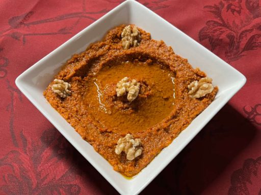 Strahlend rote Muhammara, eine würzige Paste aus gerösteter Paprika und Walnüssen, garniert mit Nüssen und Olivenöl, als vegane Spezialität.