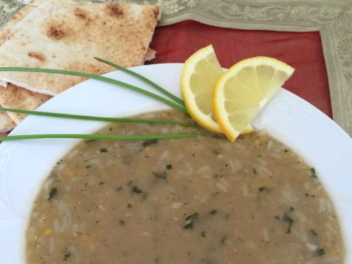 Teller mit goldener, cremiger Linsensuppe, garniert mit Kräutern.
