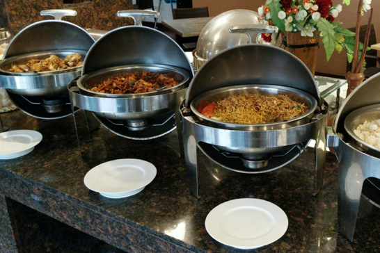 Arabisches Catering orientalische Küche mit mehreren warmen Speisen in Edelstahlschalen und weißen Tellern.