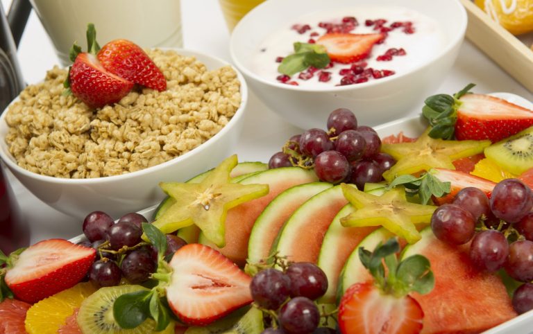 Premium-Catering Berlin mit frischem Obst, darunter Melonen, Trauben, Erdbeeren und eine Schüssel mit Müsli.