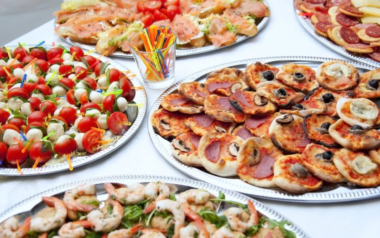 Firmenfeier-Catering mit verschiedenen Platten mit Snacks, darunter Salat, Pizza und Garnelen.