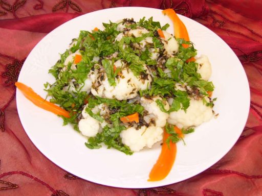 Pikanter Blumenkohlsalat mit Gewürzen und frischen Kräutern in einer Servierschale.
