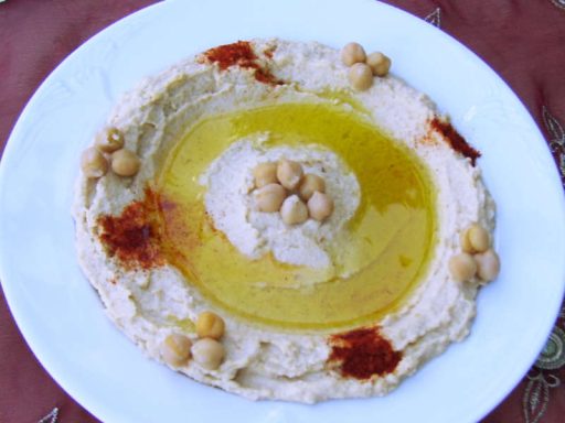 Teller mit cremigem Hummus, garniert mit Olivenöl, Paprika und Kichererbsen.