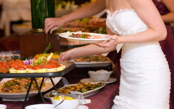 Hochzeit-Catering Berlin mit einer Braut in einem weißen Kleid vor einem Buffet.