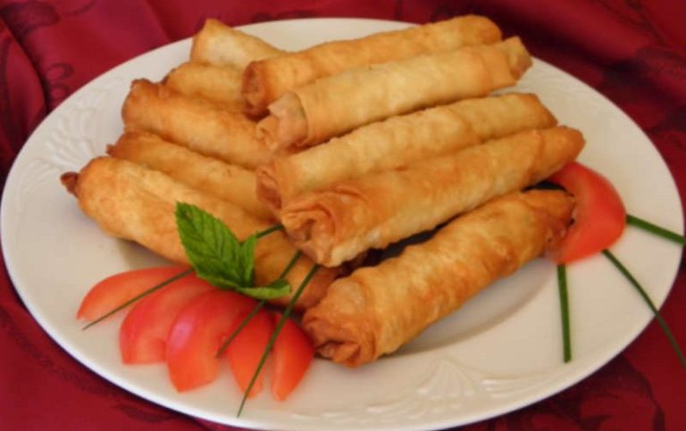 Nahaufnahme von Rukaket ma al Jibneh, einer gebackenen orientalisch-vegetarischen Teigrolle mit Käsefüllung, auf einem Mezze-Teller.
