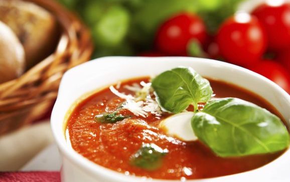 Eine dampfende Tasse europäischer vegetarischer Tomatensuppe, garniert mit frischen Kräutern