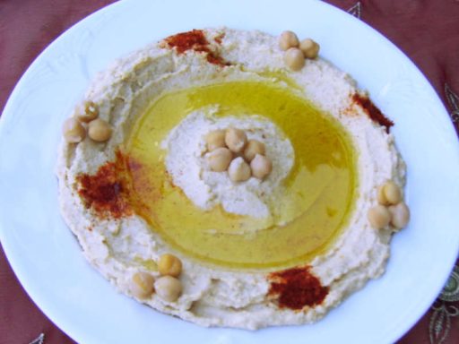Große Schale cremiger Hummus-Kichererbsen-Dip, garniert mit Olivenöl und Petersilie, als zentrale vegane Hauptkomponente für Ihr Event.